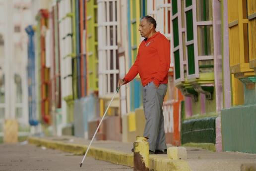 A visually impaired man walks with a cane.