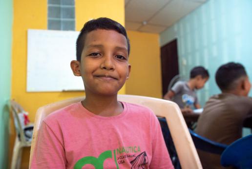 Un niño con camisa rosada sentado en una silla sonríe a la cámara.