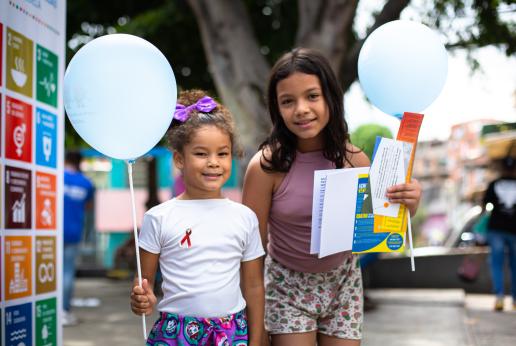 Dos niñas sonríen a la cámara sosteniendo varios folletos y un globo.