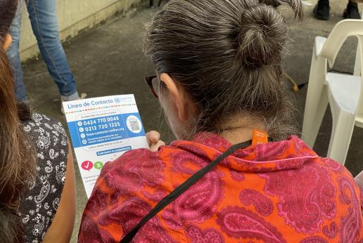 Una mujer de espalda a la cámara lee un folleto de la Línea de Contacto de Naciones Unidas en Venezuela.