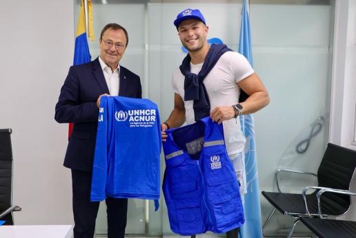 Un hombre con discapacidad y el representante de ACNUR sostienen una franela.