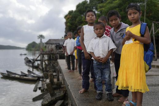 Un grupo de niños y niñas indígenas esperan en fila junto a la orilla de un río. 