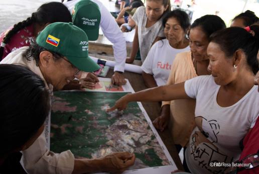 Grupo de mujeres indígenas y personal de FAO reunidos revisando un mapa.