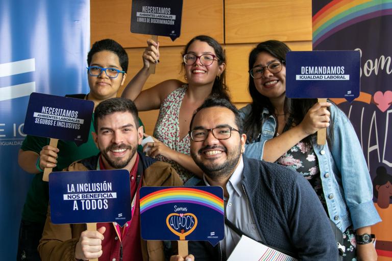 Un grupo de jóvenes sostiene pancartas sobre derechos de las personas LGBTIQ+ y la igualdad laboral.