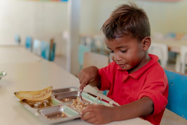 Un niño come un plato de comida caliente en la escuela.