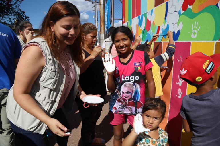 Una mujer y dos niñas pintan un mural.