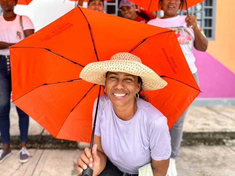 Una mujer sonríe a cámara con un paraguas naranja.