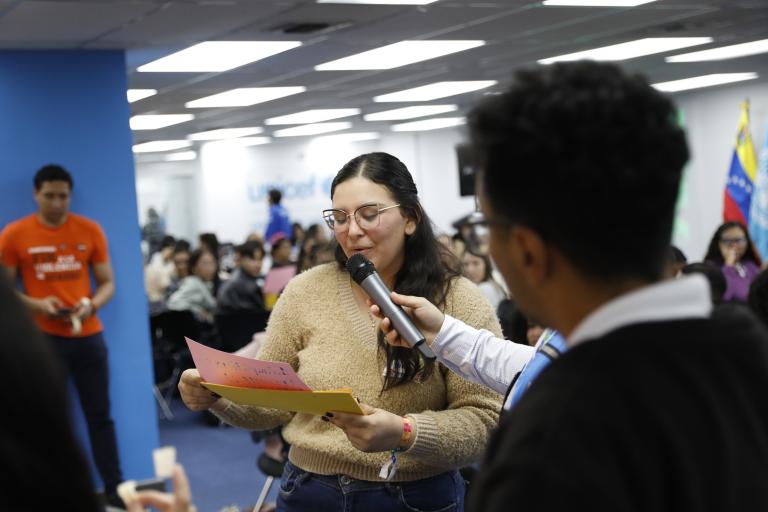 Una joven lee una tarjeta en voz alta frente a un micrófono.